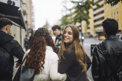 Portrait of smiling girl looking over shoulder while walking with friends at street