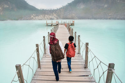 Rear view of siblings walking on pier over lake