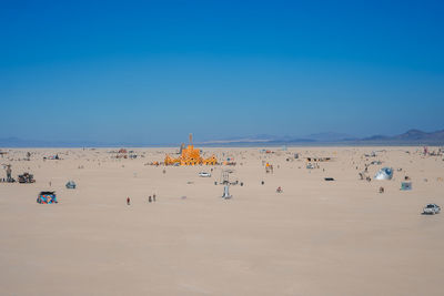 People at beach against clear blue sky