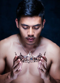 Shirtless young man holding crown against black background