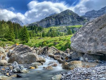 Stream flowing through rocks against sky
