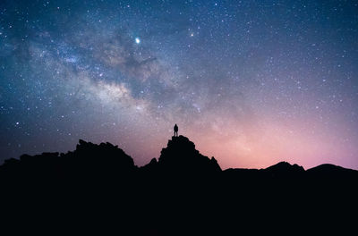 Silhouette of man of hikers standing on dark rock against starry night sky in long exposure in tenerife