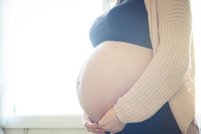 Midsection of pregnant woman standing at home