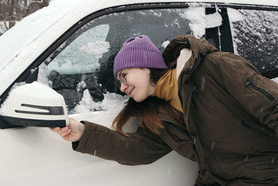 Young woman in warm clothes by the car in winter