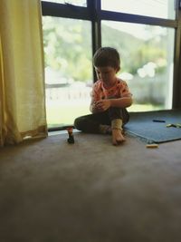 Boy playing with toy by glass window at home