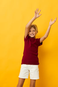 Portrait of young woman with arms raised standing against yellow background