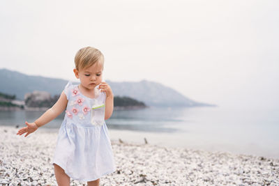 Full length of cute girl standing on sea shore against sky