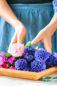 Midsection of woman holding flowers in tray on table