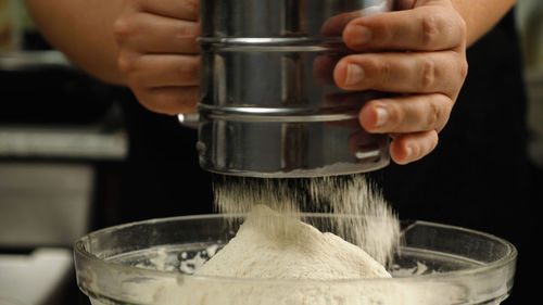 Close-up of a cook sifting flour through a metal sieve into a glass bowl. the concept of the bakery