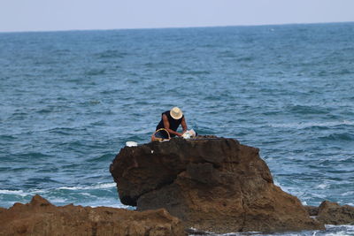 Fisherman standing on rock by sea against sky