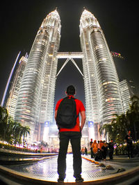 Rear view of man standing at illuminated city against sky at night