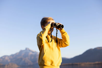 Boy looking through binoculars against sky