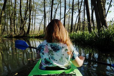 Rear view of woman canoeing on lake at forest