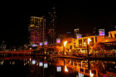 Illuminated buildings by river against sky at night