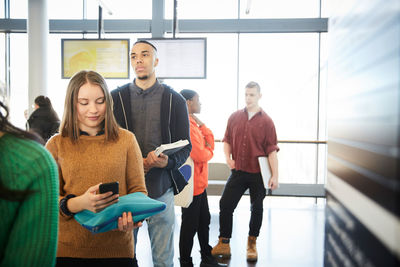 Young male and female students standing in row at university lobby