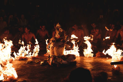 Man surrounded by fire and people during traditional festival at night