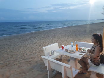 Woman sitting on table by sea against sky