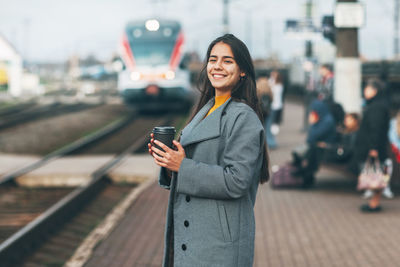 Portrait of smiling young woman using phone while standing on road