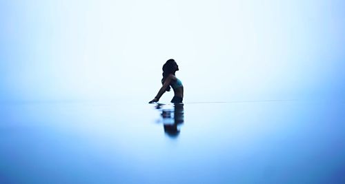 Side view of woman in sea against blue sky