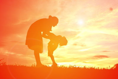 Side view of silhouette woman playing with child on field against sky during sunset