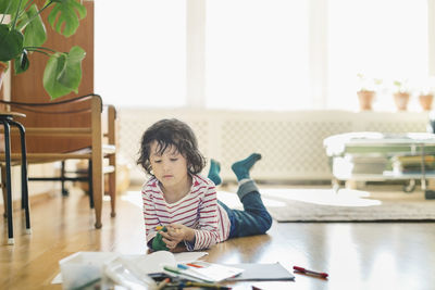 Boy with colorful felt lip pens and books lying on floor at home