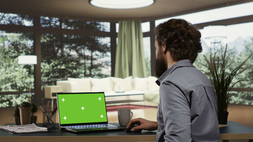 Side view of young man using laptop while standing in cafe