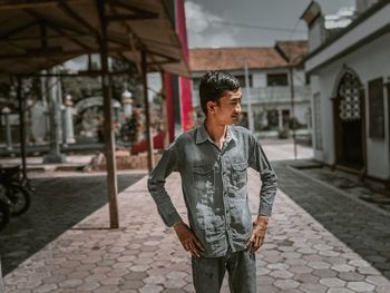 Young man looking away while standing on street in city