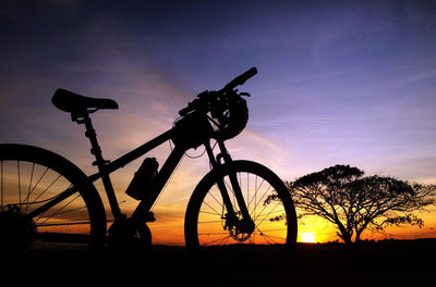 Silhouette bicycle on field against sky at sunset