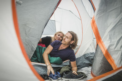 Couple peeking though tent while leaning in sleeping bag during camping