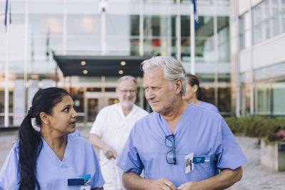 Multiracial male and female doctors in scrubs walking outside hospital