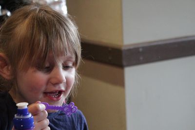Close-up of smiling girl holding bubble wand at home