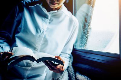 Midsection of woman reading book by window