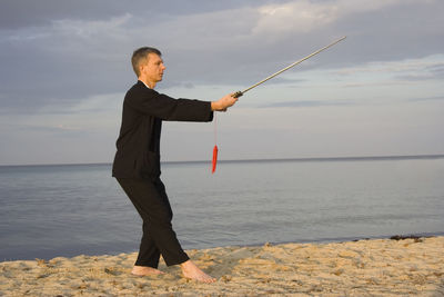 Man practicing tai chi at beach against cloudy sky