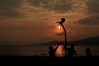 Silhouette people on beach against sky during sunset