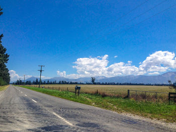 Road amidst field against blue sky