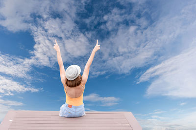 Rear view of woman sitting on observation point against cloudy sky