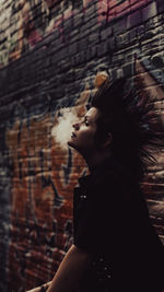 Side view of young woman looking away against wall