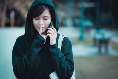 Smiling young woman with finger on lips listening to mobile phone