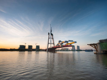 Cranes at commercial dock against sky during sunset