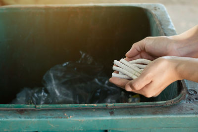 Close-up of hand holding cigarettes over garbage bin