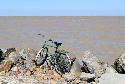 Bicycle on rock by sea against clear sky