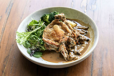 High angle view of chicken with mushroom sauce in serving dish on wooden table