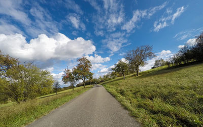 Road amidst trees on field against sky