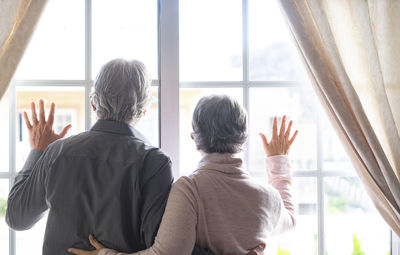 Rear view of man and woman looking through glass window at home