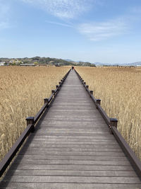 View of wooden walkway in field against sky