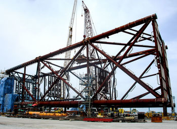 Low angle view of cranes at construction site against sky