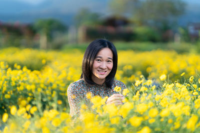 Portrait of smiling young woman with yellow flower in field