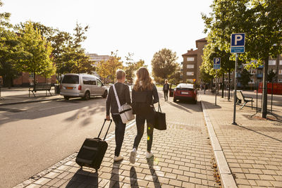 Rear view of siblings with suitcase walking on roadside