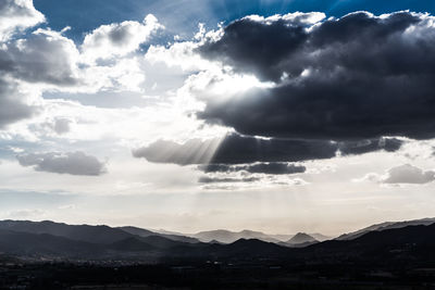 Sunlight streaming through clouds over silhouette mountains