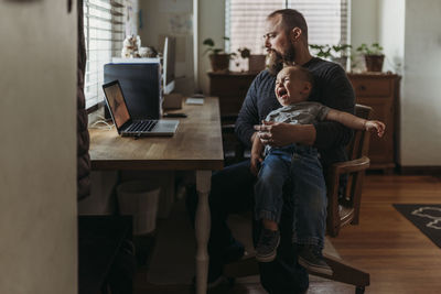 Father trying to work from home with toddler tantrum in his lap